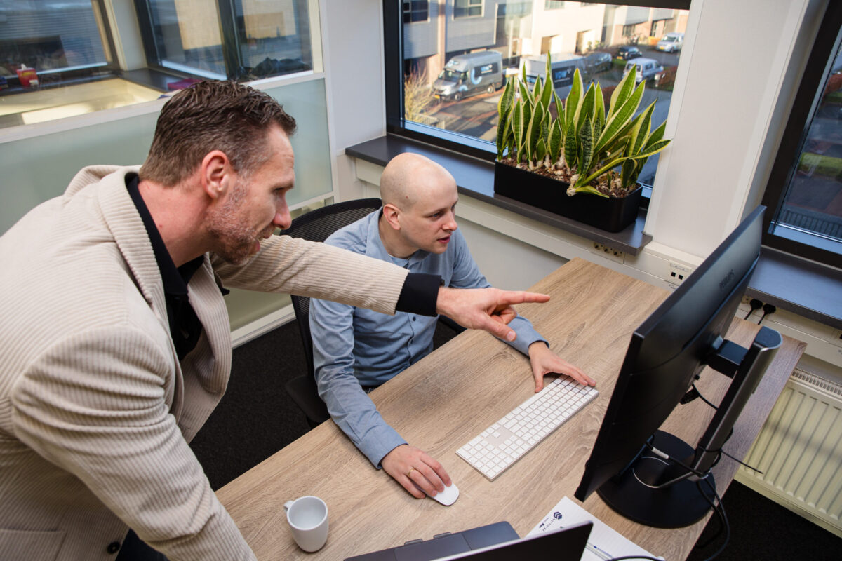 Two people behind a computer. One is pointing to the screen.