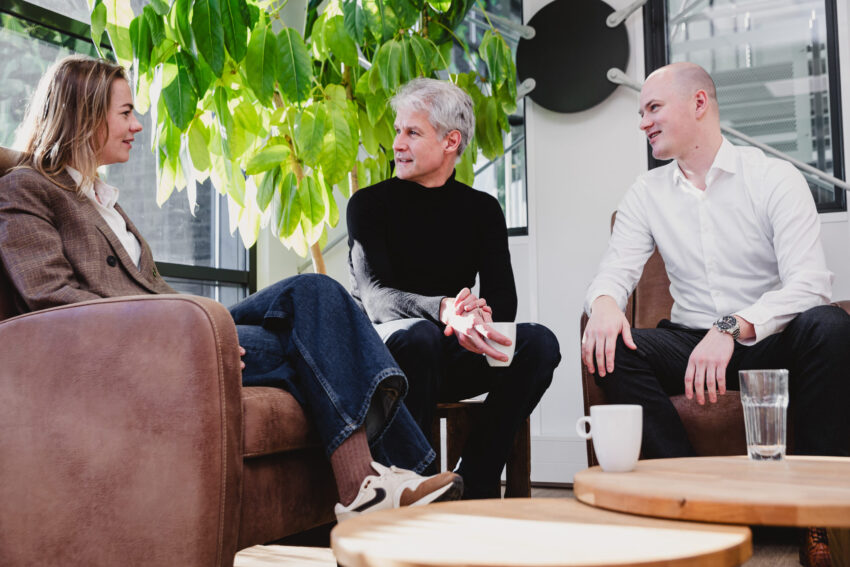 Three people sitting in chairs having a conversation. Plant in the background.