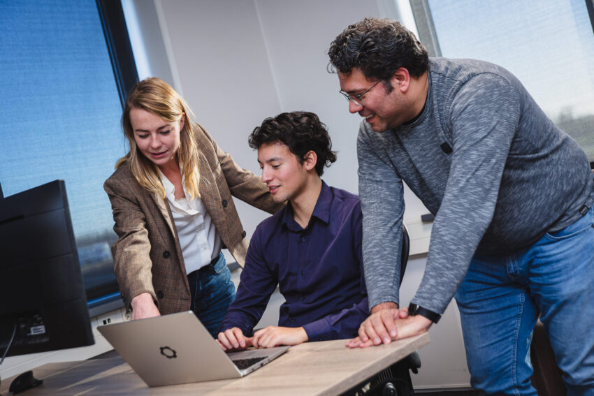 Three people behind a desk looking at a laptop.