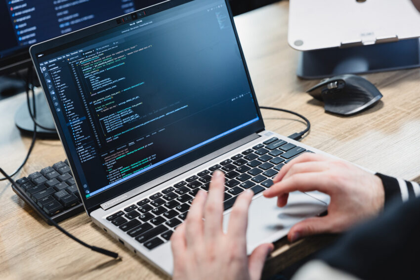 A laptop with lines of code, with hands above the keyboard.