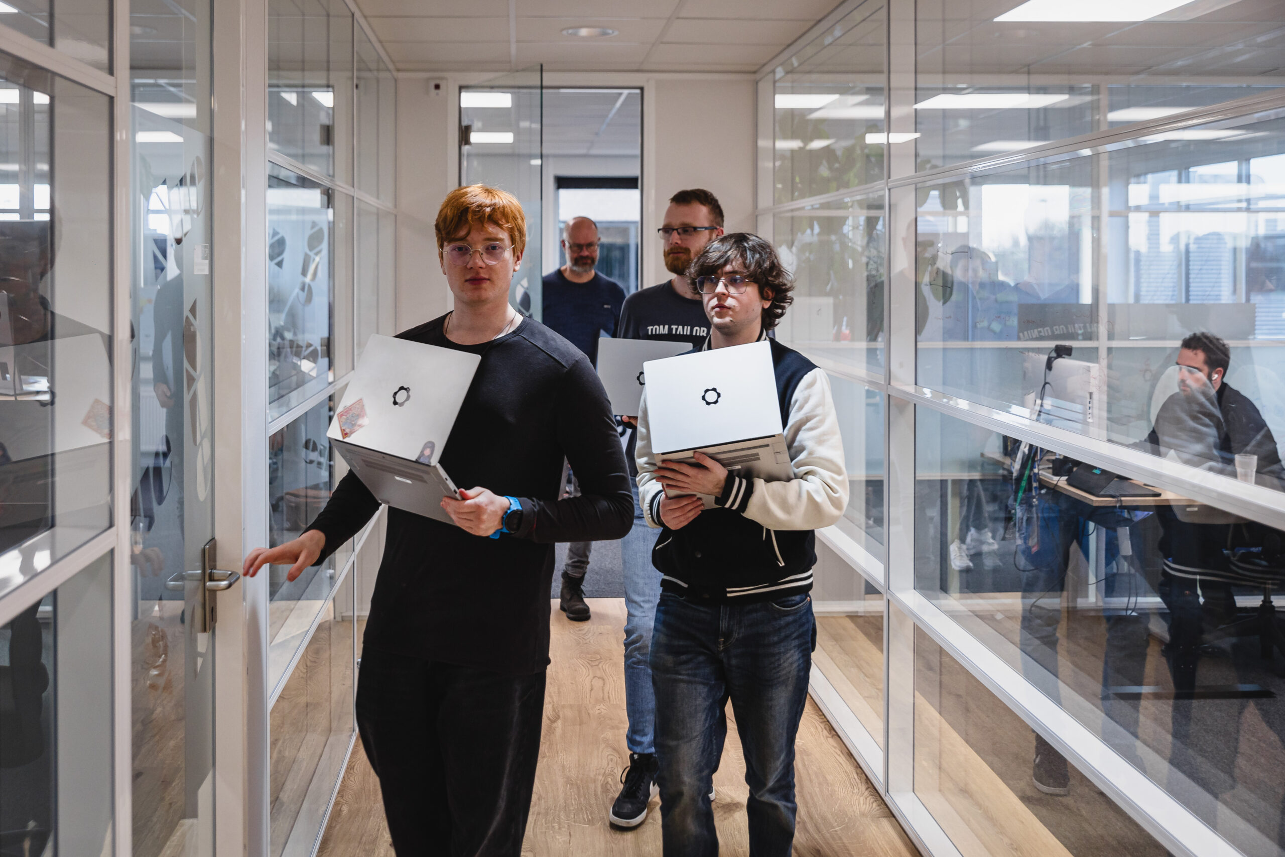 A group of people with laptops in their hands walking trough an office hallway.