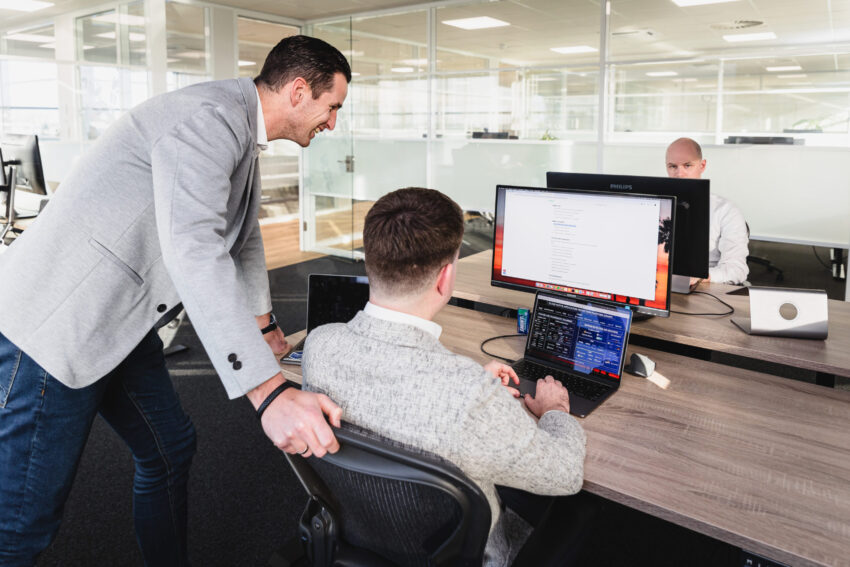 Two people looking at a computer screen, one sitting and one standing.
