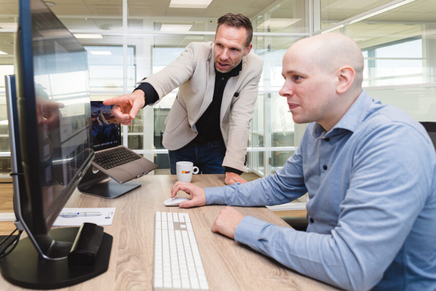 Two people looking at a computer screen. One sitting and one standing.