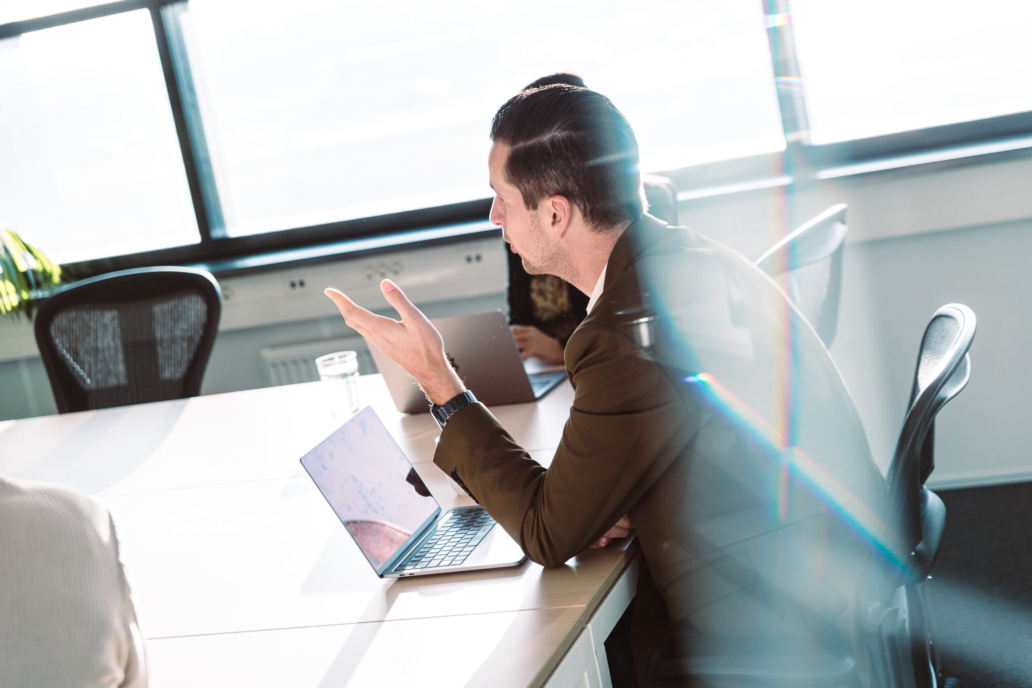 People in a meeting room with a laptop on the table, seen through glass.